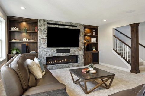 Finished basement with a stone fireplace, built-ins, and a media wall, by MDR Design-Build-Remodel